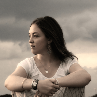A girl sitting indian style looking to her right off in the distance